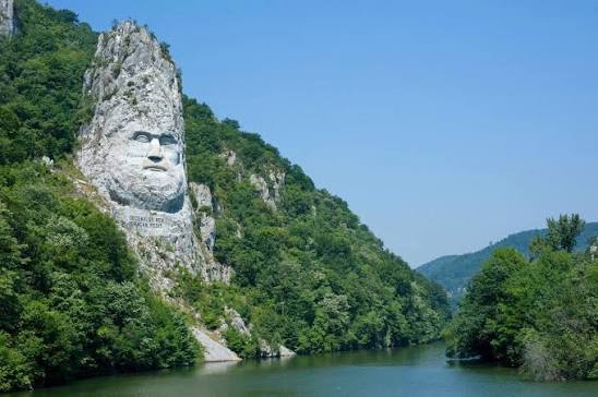 Carved face of Decebalus above the Danube between forested cliffs
